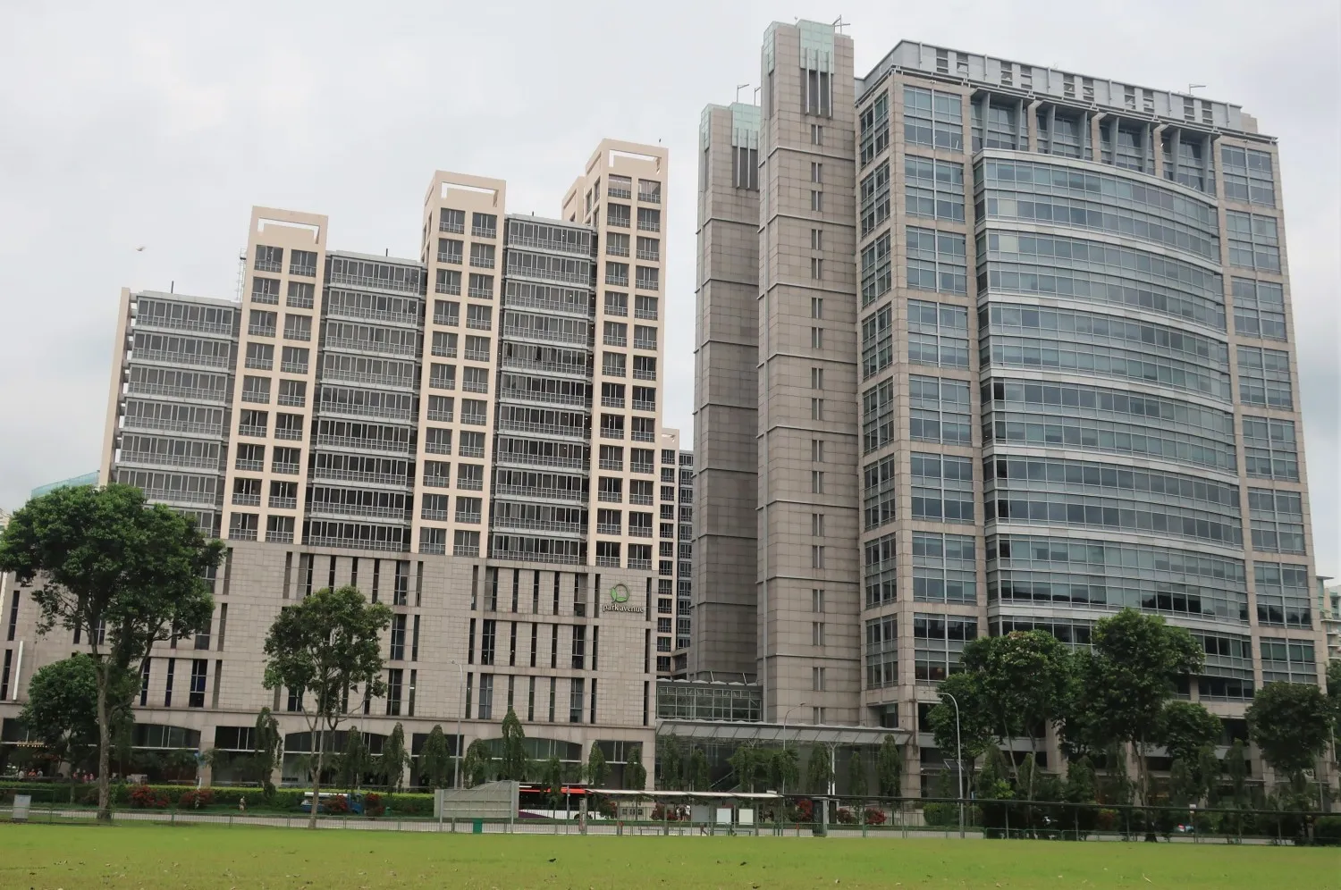 Modern multi-story office buildings at UE Square with glass windows and beige concrete facades behind a grassy park area with trees.